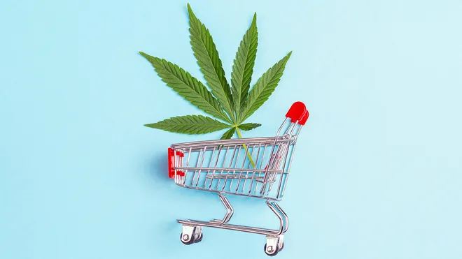 Single cannabis leaf in a miniature shopping cart on a blue background